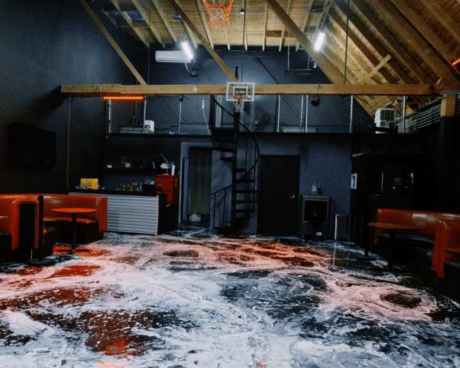 The image shows a large indoor space with red seating, a basketball hoop, and a floor covered in a foamy substance.