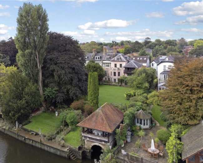 The image shows a riverfront property featuring multiple houses with extensive gardens and trees.