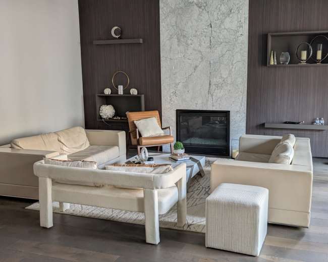 The image shows a modern living room with a minimalist design, featuring two sofas, a coffee table, an armchair, and a wall-mounted fireplace.