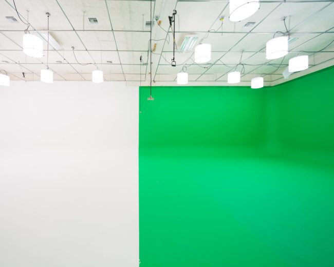 A studio space divided into two sections, one with a white wall and the other with a green wall, illuminated by overhead lights.