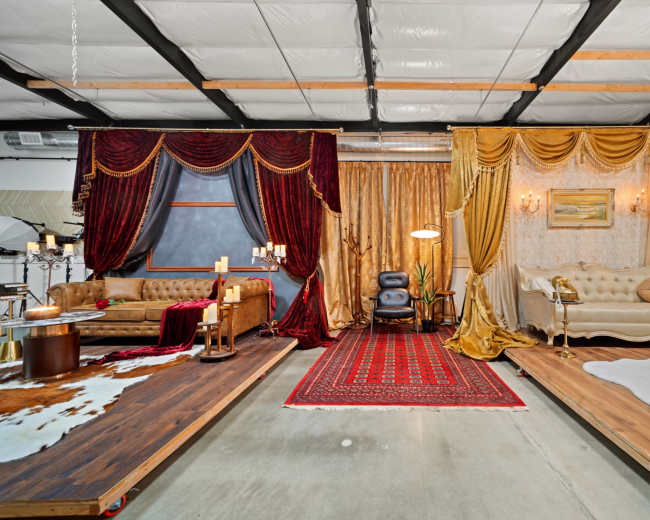 The image shows a split interior space featuring two distinct lounge areas, one adorned with red velvet drapes and ornate décor, and the other with gold curtains and elegant furniture.