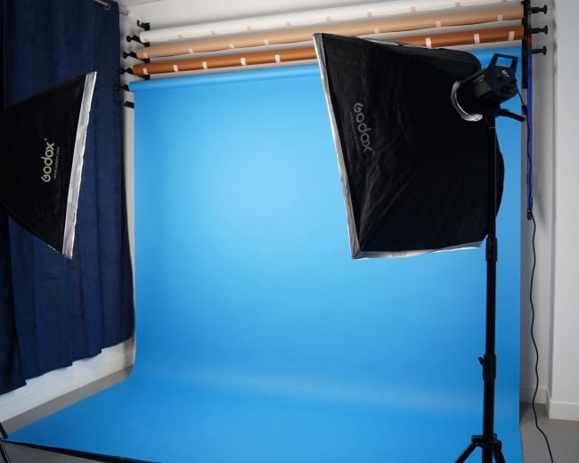 The image shows a photography studio setup with two softbox lights positioned on either side of a vibrant blue backdrop.