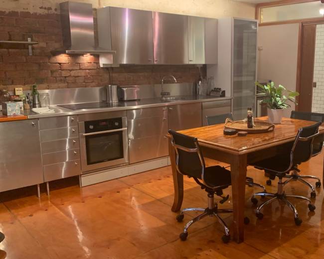 The image shows a modern kitchen with stainless steel appliances and a wooden dining table surrounded by black chairs.