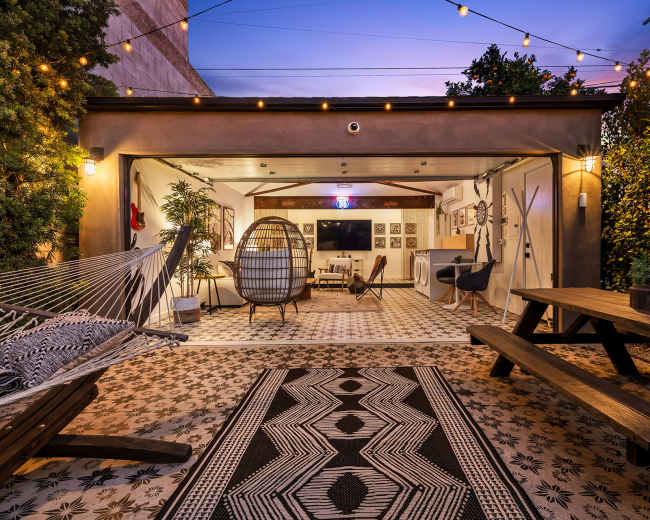 The scene features a cozy outdoor space with a hammock, a hanging chair, a picnic table, and decorative string lights under a twilight sky.