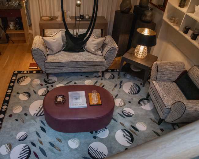 The image depicts a cozy living room with a rug featuring circular patterns, a central ottoman, and two comfortable sofas arranged around a coffee table.