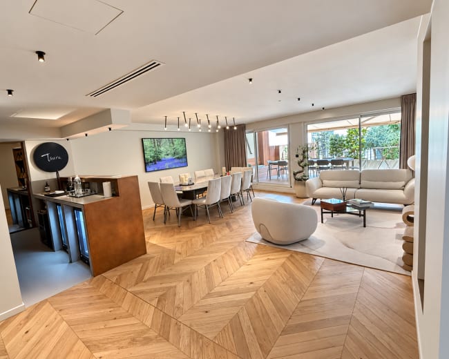 The image shows an elegantly designed open-plan living and dining area with modern furniture and large windows allowing natural light.