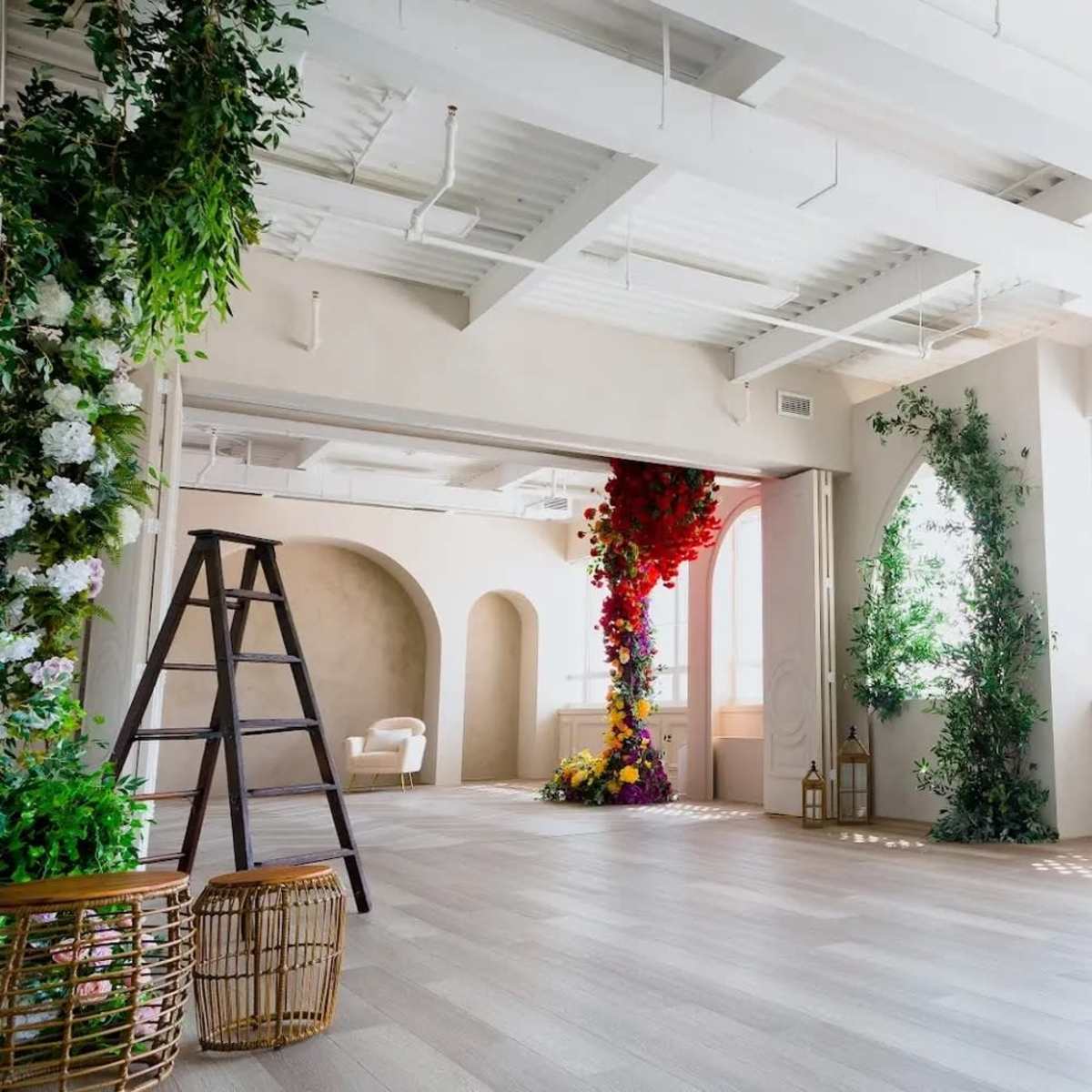 A bright, modern interior space with large windows, decorated with floral arrangements and a ladder positioned in one corner.