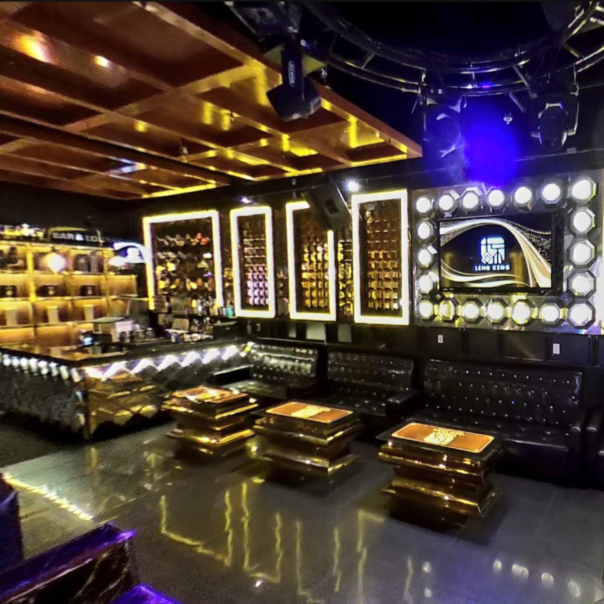 A modern lounge with black leather seating, illuminated gold accents, and a large screen framed by decorative panels.