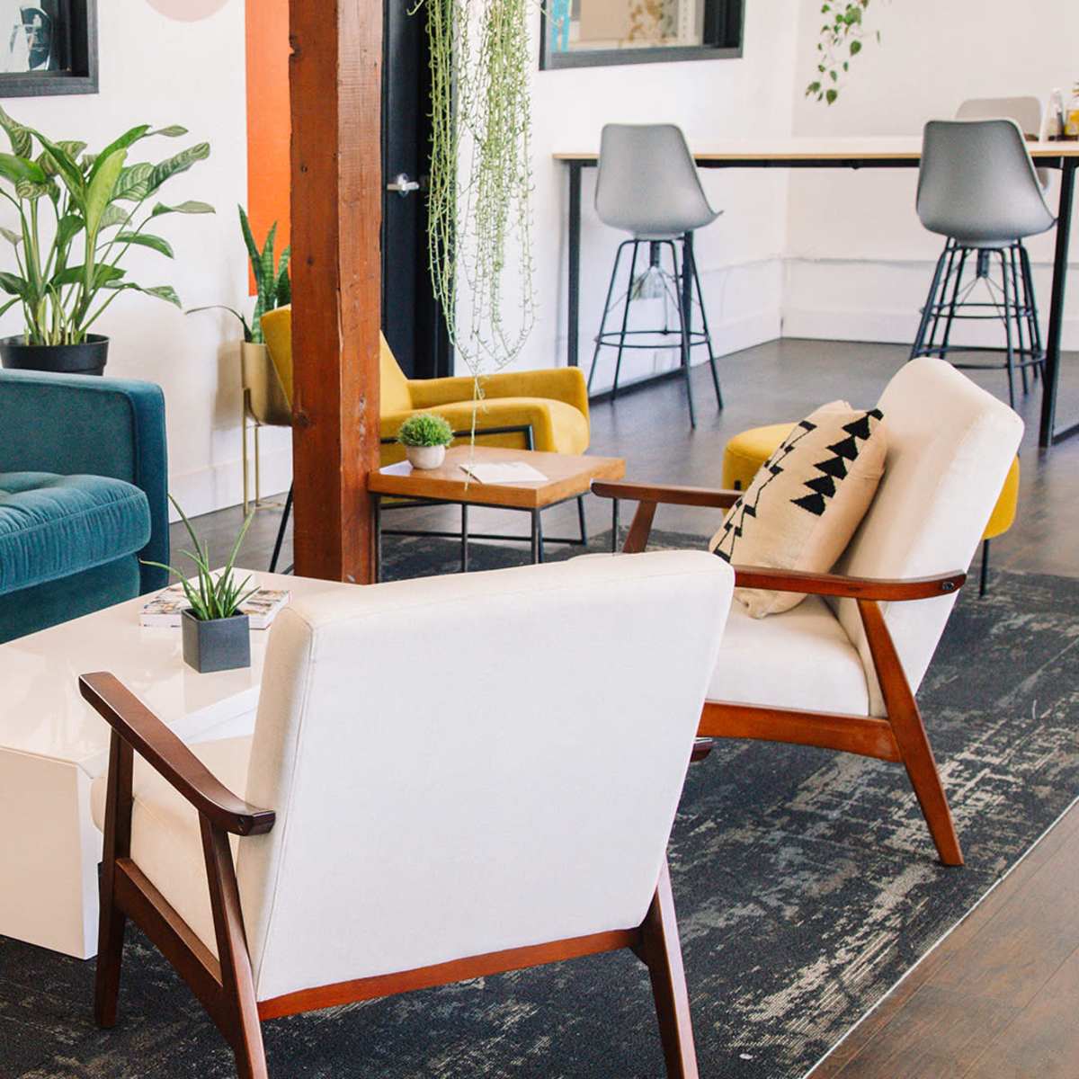 A modern seating area with a blue couch, two white armchairs, a coffee table, and green plants, set against a backdrop of light-colored walls and wooden accents.