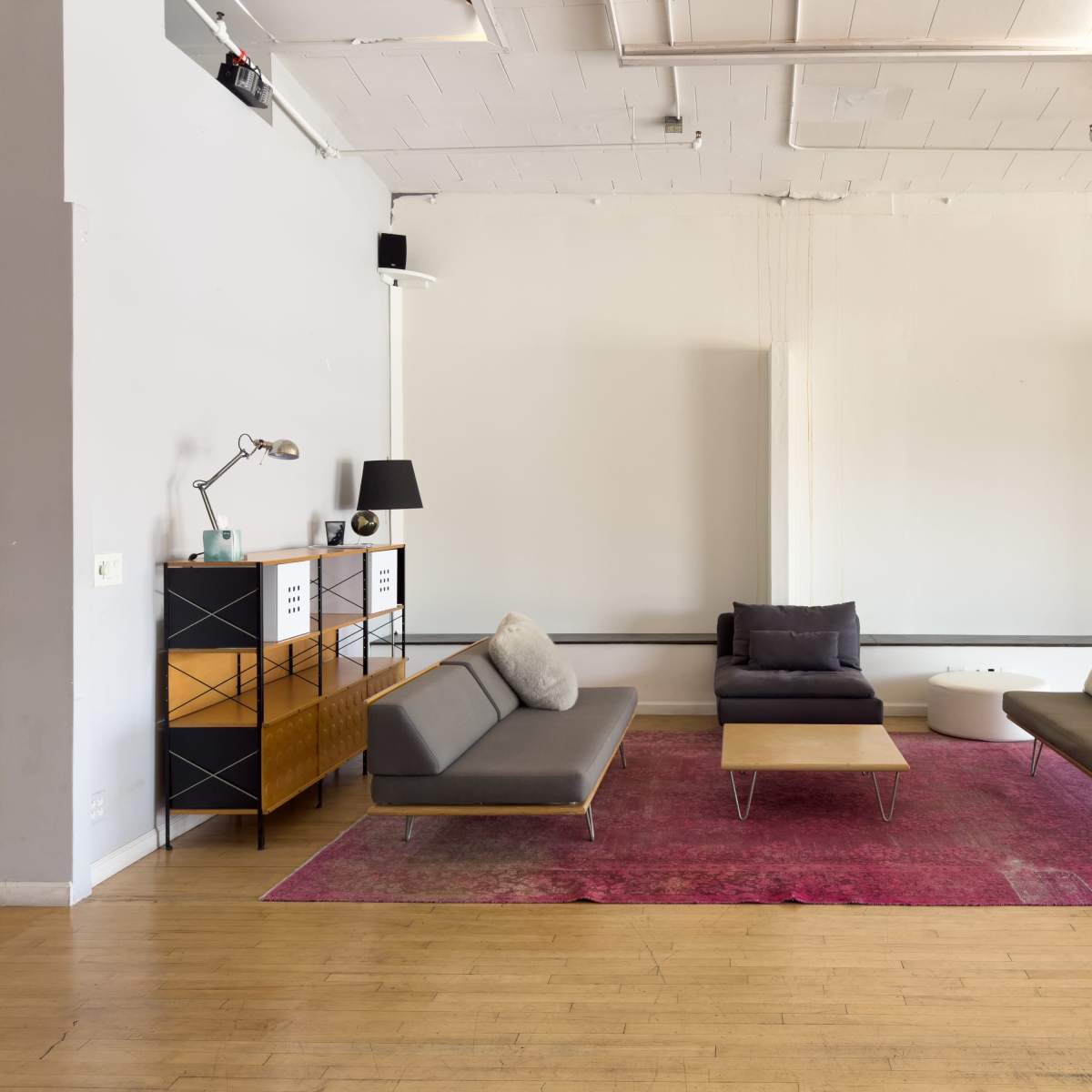 A modern living space with gray sofas arranged around a central coffee table on a pink area rug, complemented by a sideboard and a floor lamp.