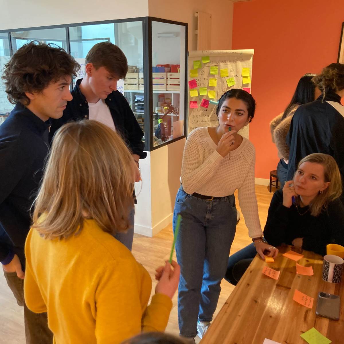 A group of young adults engages in a discussion around a table filled with sticky notes in a brightly lit workspace.
