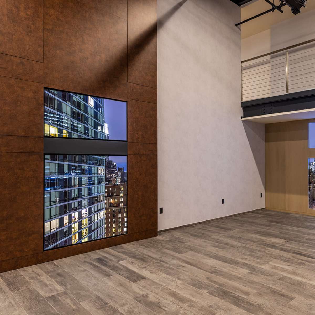 A modern interior room with large windows revealing a city skyline at night, featuring wooden flooring and a minimalist design.