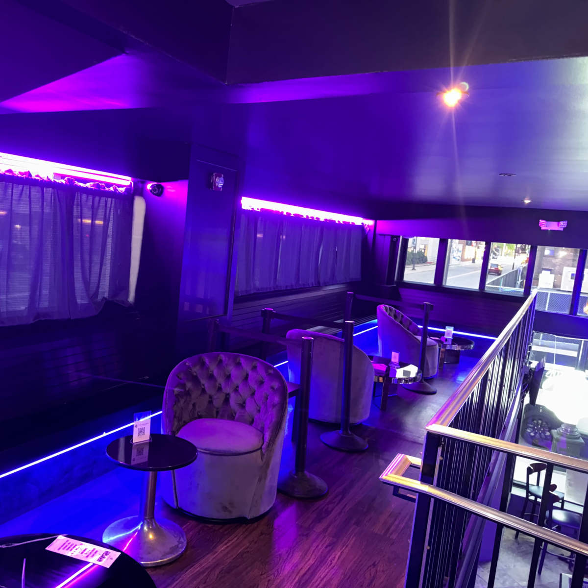 A dimly lit lounge area with purple lighting, featuring two plush chairs and small tables along the walls.