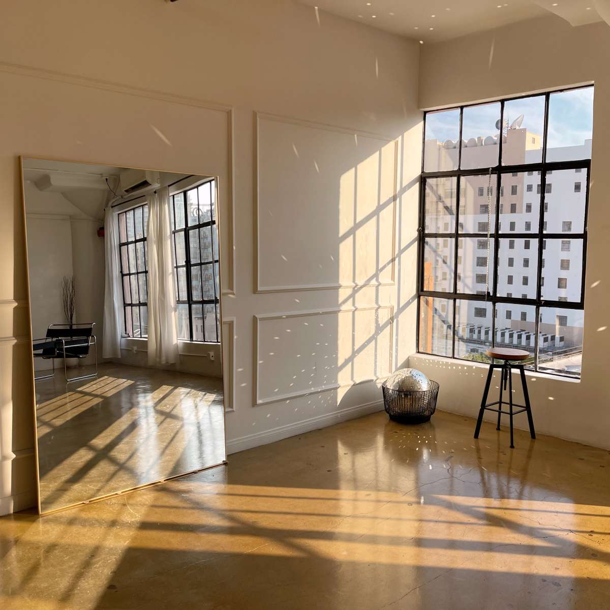 A brightly lit interior space with large windows, a full-length mirror, and a stool beside a decorative globe.
