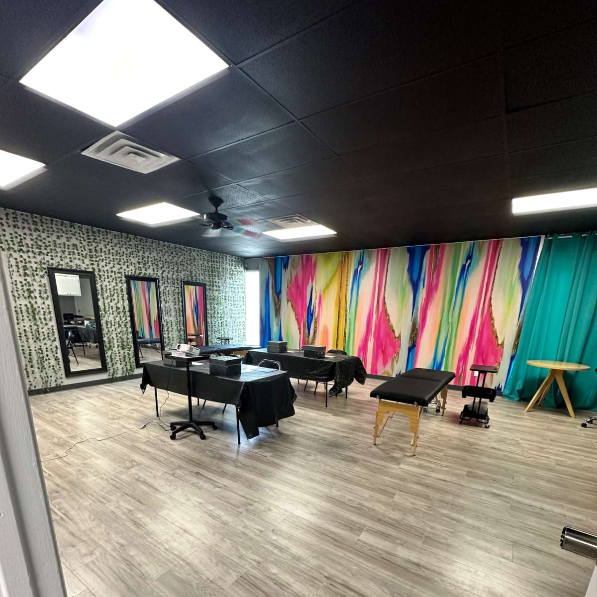 A spacious, brightly colored treatment room with wooden flooring, equipped with multiple tables covered in black cloth and vibrant wall art.