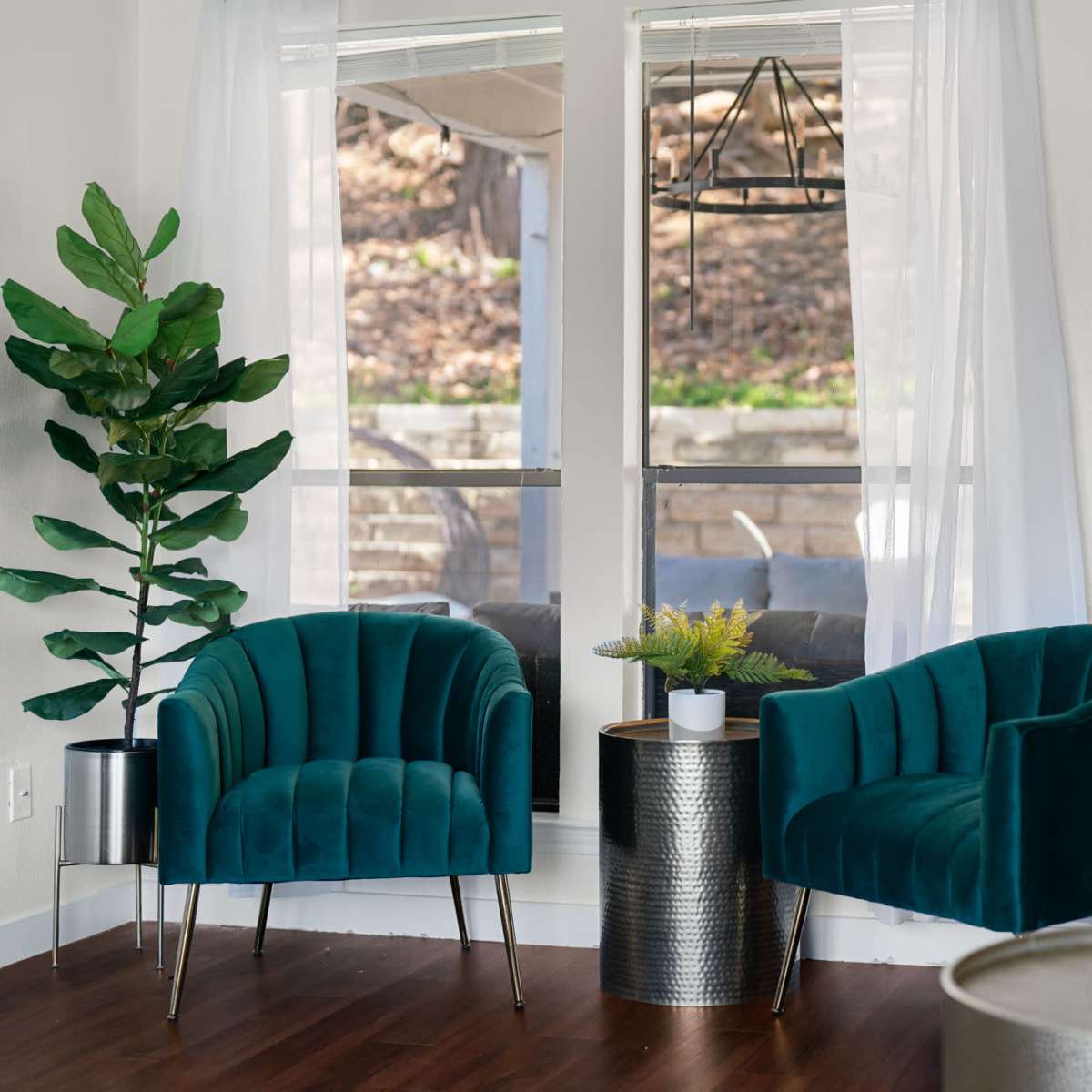 A modern interior with two green upholstered chairs, a small round table, and large windows allowing natural light.
