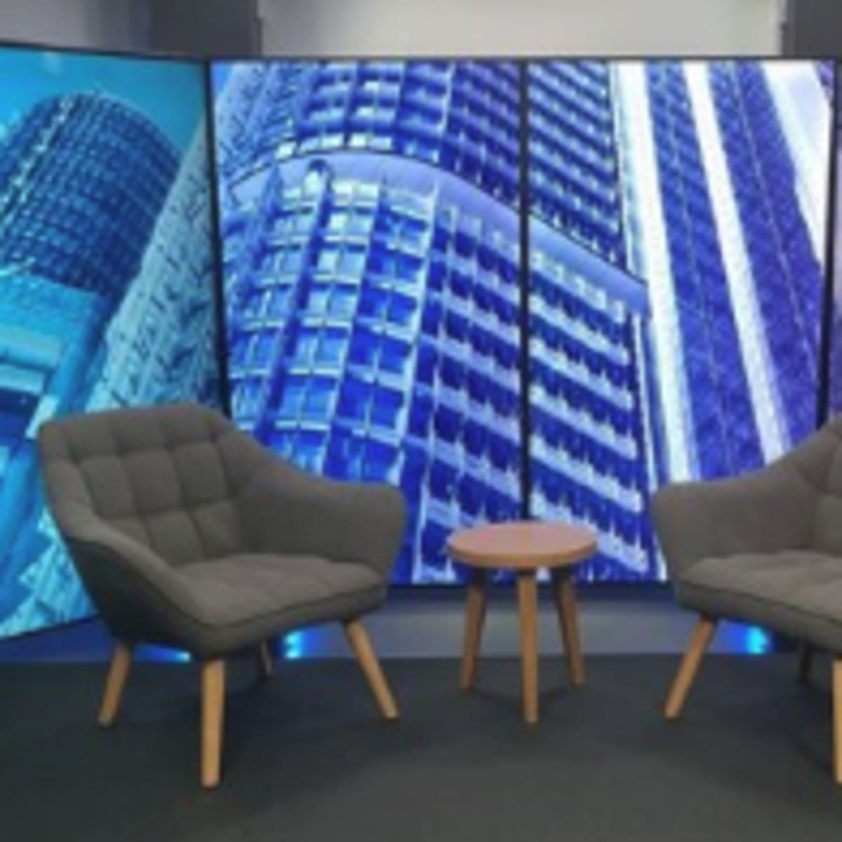 A modern studio set with two gray upholstered chairs facing a small wooden table, surrounded by backdrop panels featuring skyscraper images.