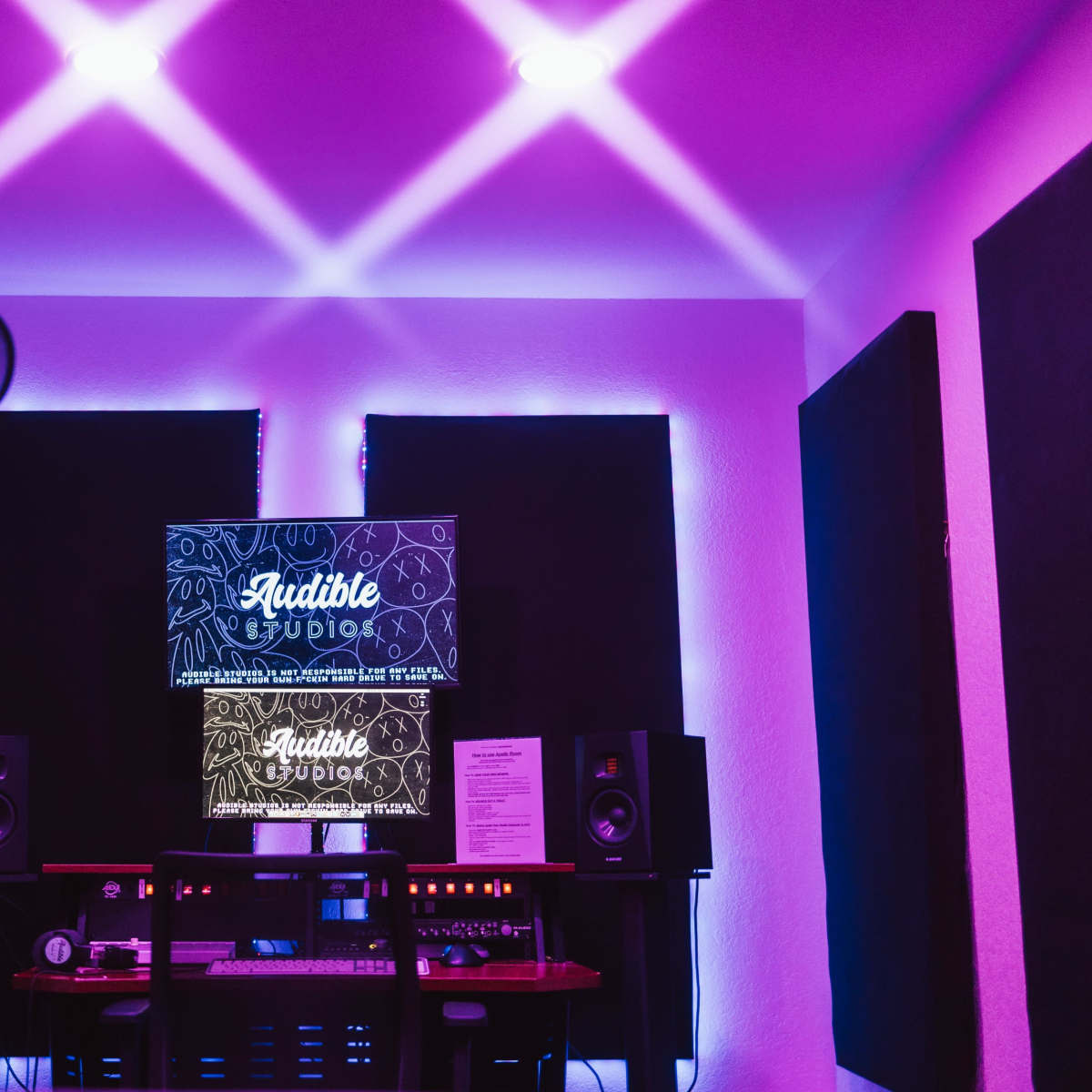 A recording studio with purple lighting, featuring soundproof panels, a microphone, and audio equipment.