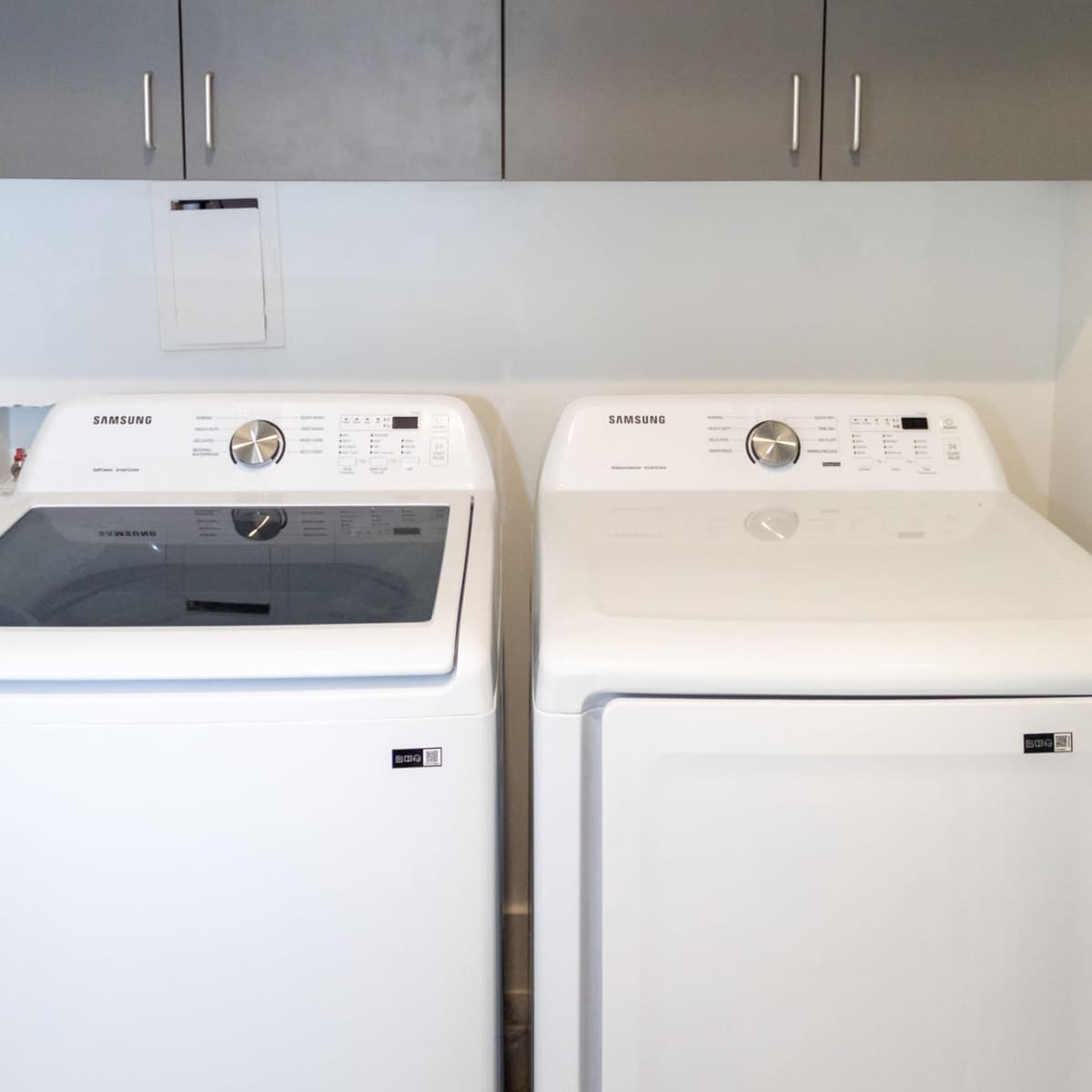 A side-by-side arrangement of a top-loading washer and a front-loading dryer beneath dark gray cabinets.