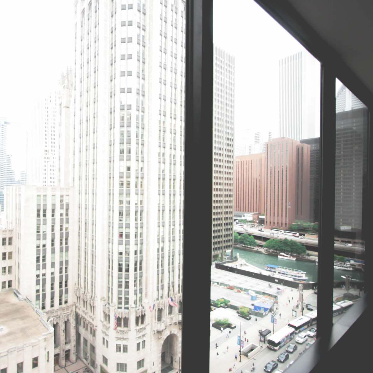 A cityscape view from a window, featuring a mix of tall buildings, including a prominent skyscraper, and a busy street below.
