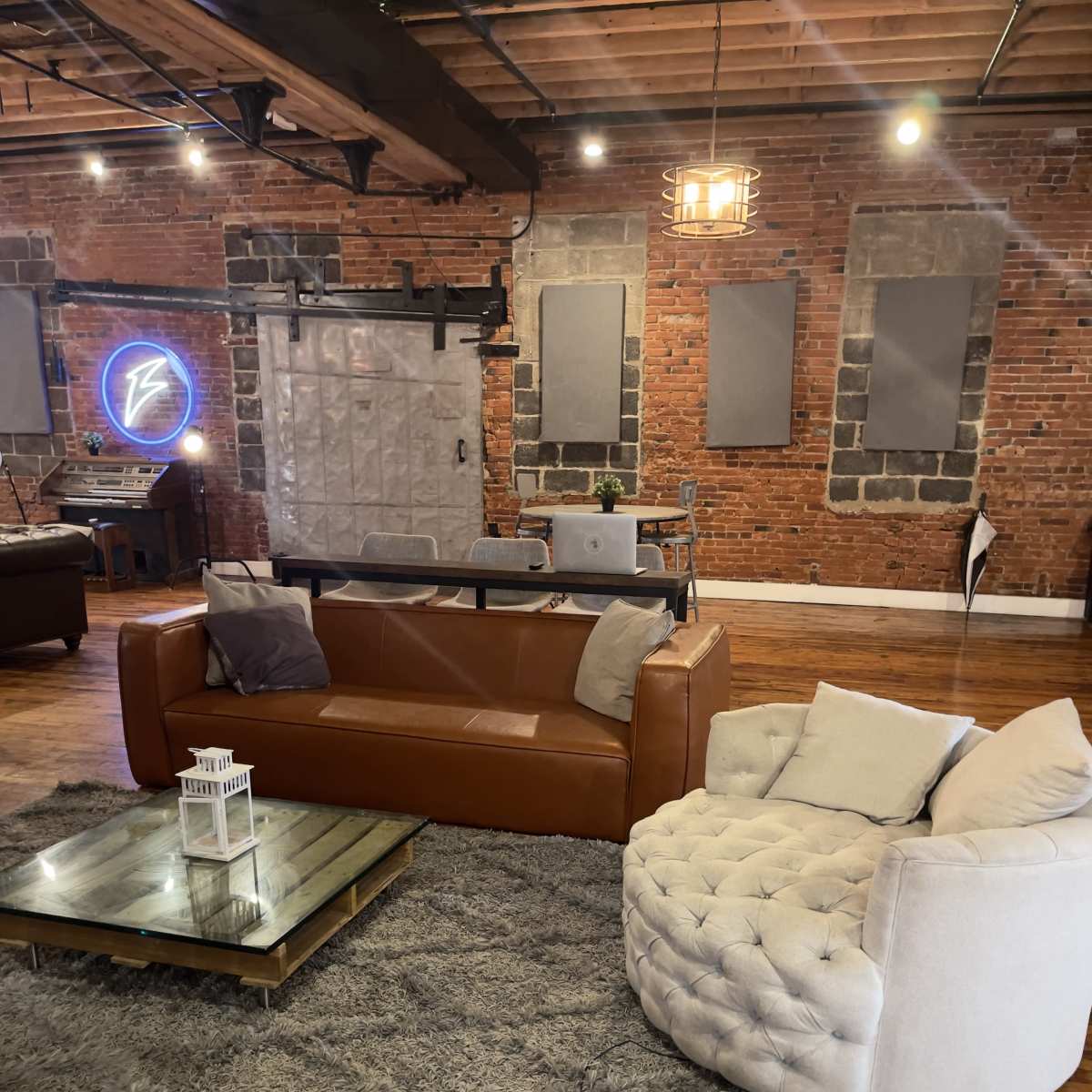 A modern living space with a brown leather sofa, a round white tufted chair, a glass coffee table on a gray rug, and exposed brick walls.