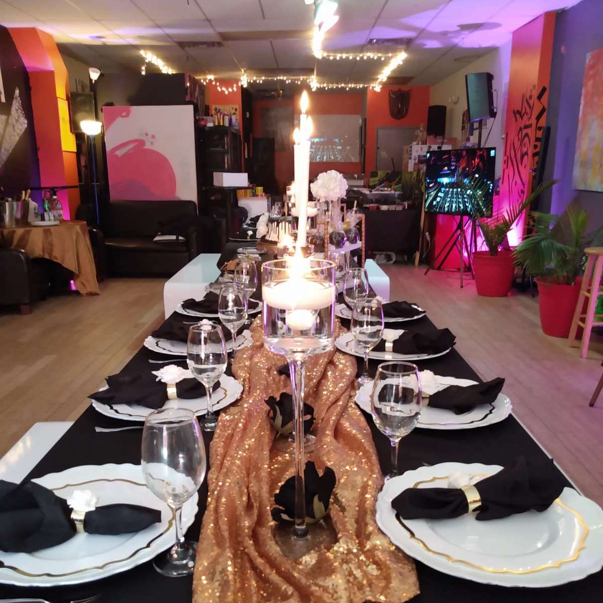 A long dining table is set with elegant place settings, a golden table runner, and a lit candle in the center.