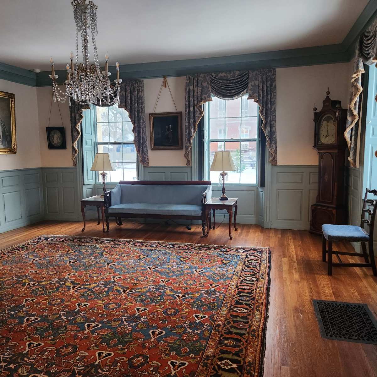 The room features a blue sofa, two lamps, a large area rug, and various framed artworks on the walls.