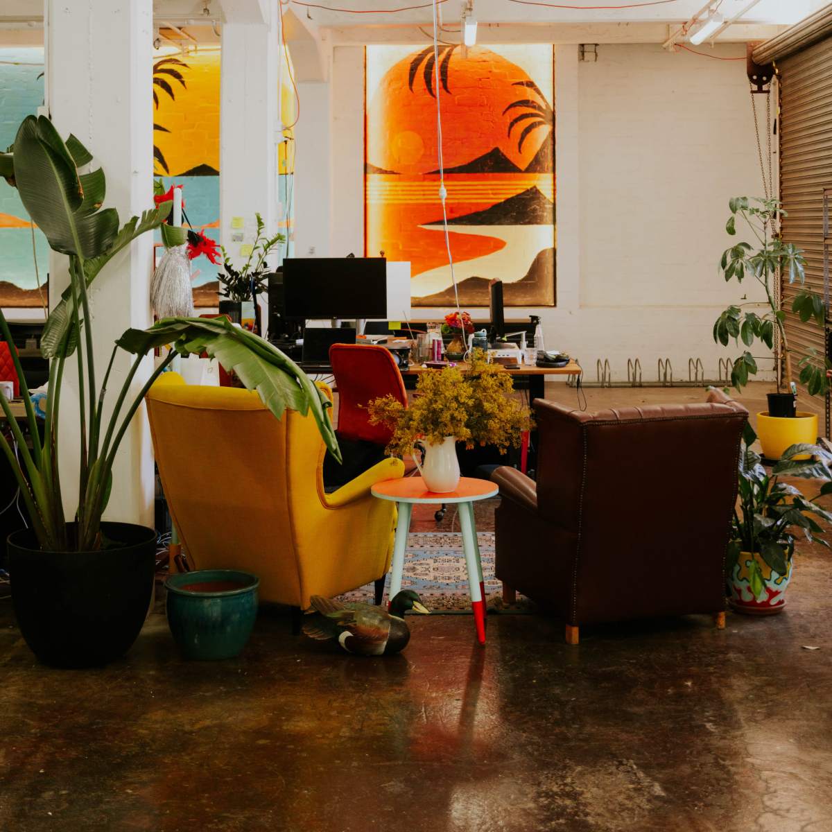 A stylish workspace with colorful chairs, plants, and large abstract artwork on the walls.