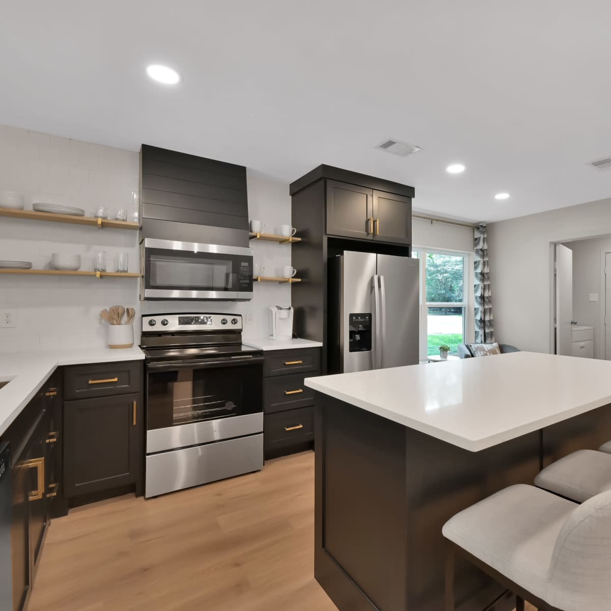 A modern kitchen with stainless steel appliances, dark cabinetry, a white countertop, and a central island with seating.