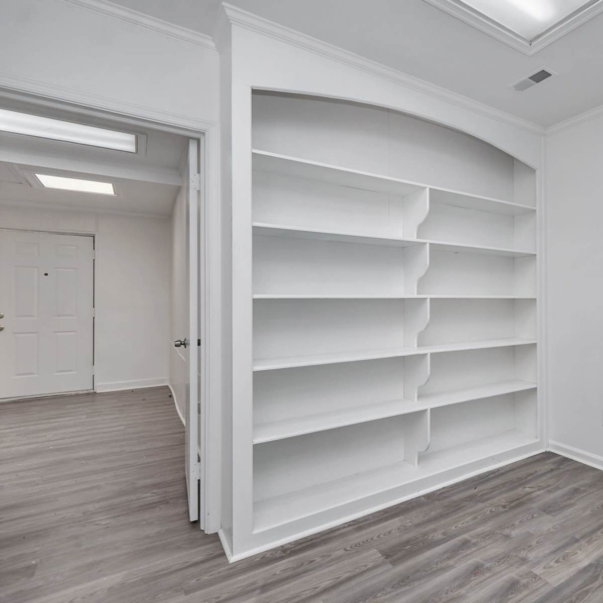 A room with a large white built-in shelving unit against one wall and a door leading to another room.