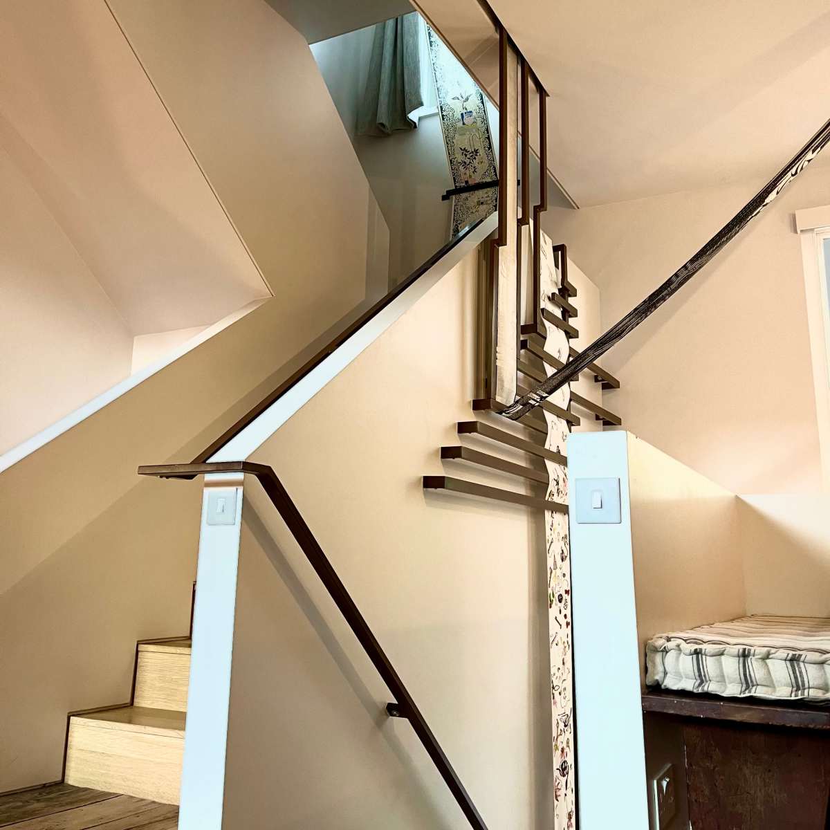 A staircase with an angular design leads to an upper level, featuring wooden steps and metal railings, illuminated by natural light.