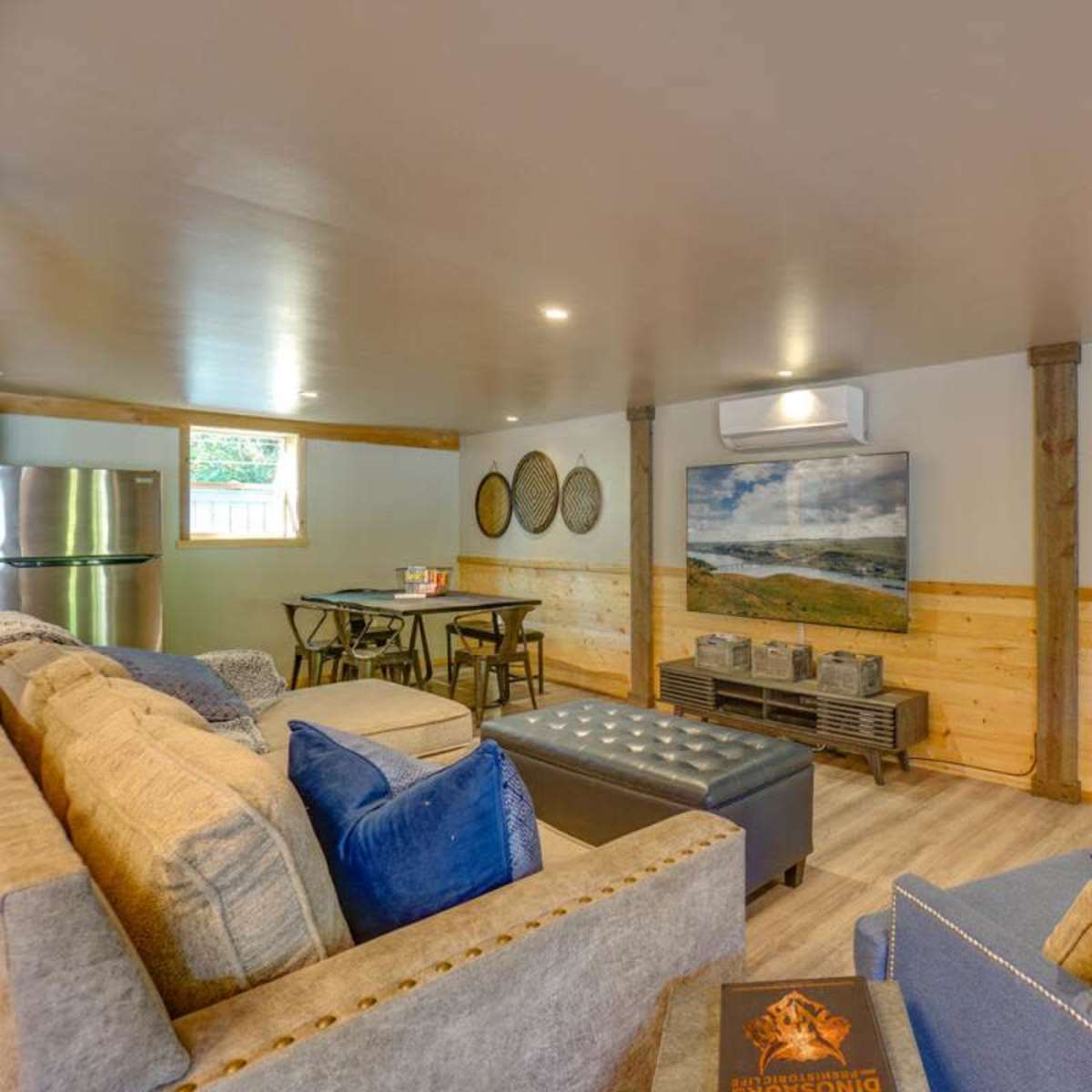 A modern, open living space featuring a sectional sofa, a coffee table, a television, and a dining area with two chairs and a table.