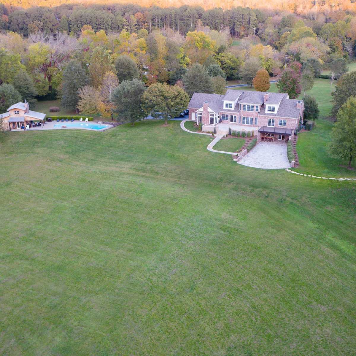 A large residential property with a two-story house, a swimming pool, and a separate building surrounded by lush greenery and trees.