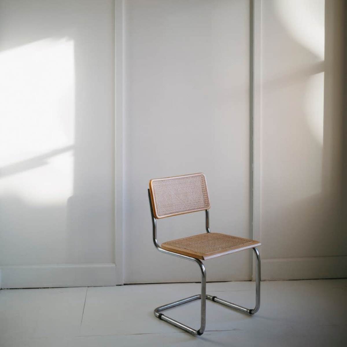A minimalistic room features a single metal-framed chair positioned in front of a white door.