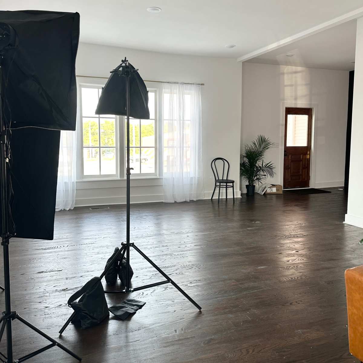 A spacious room with wooden floors, large windows, and professional lighting equipment set up.