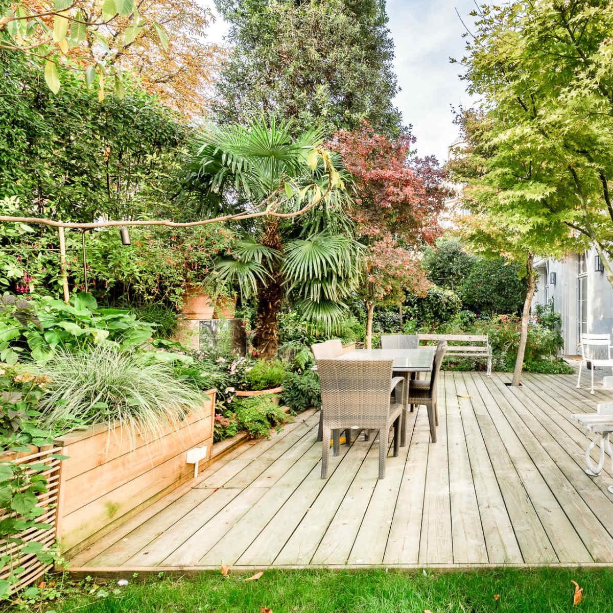 A wooden deck surrounded by lush greenery and trees, with a dining table and chairs situated on one side.