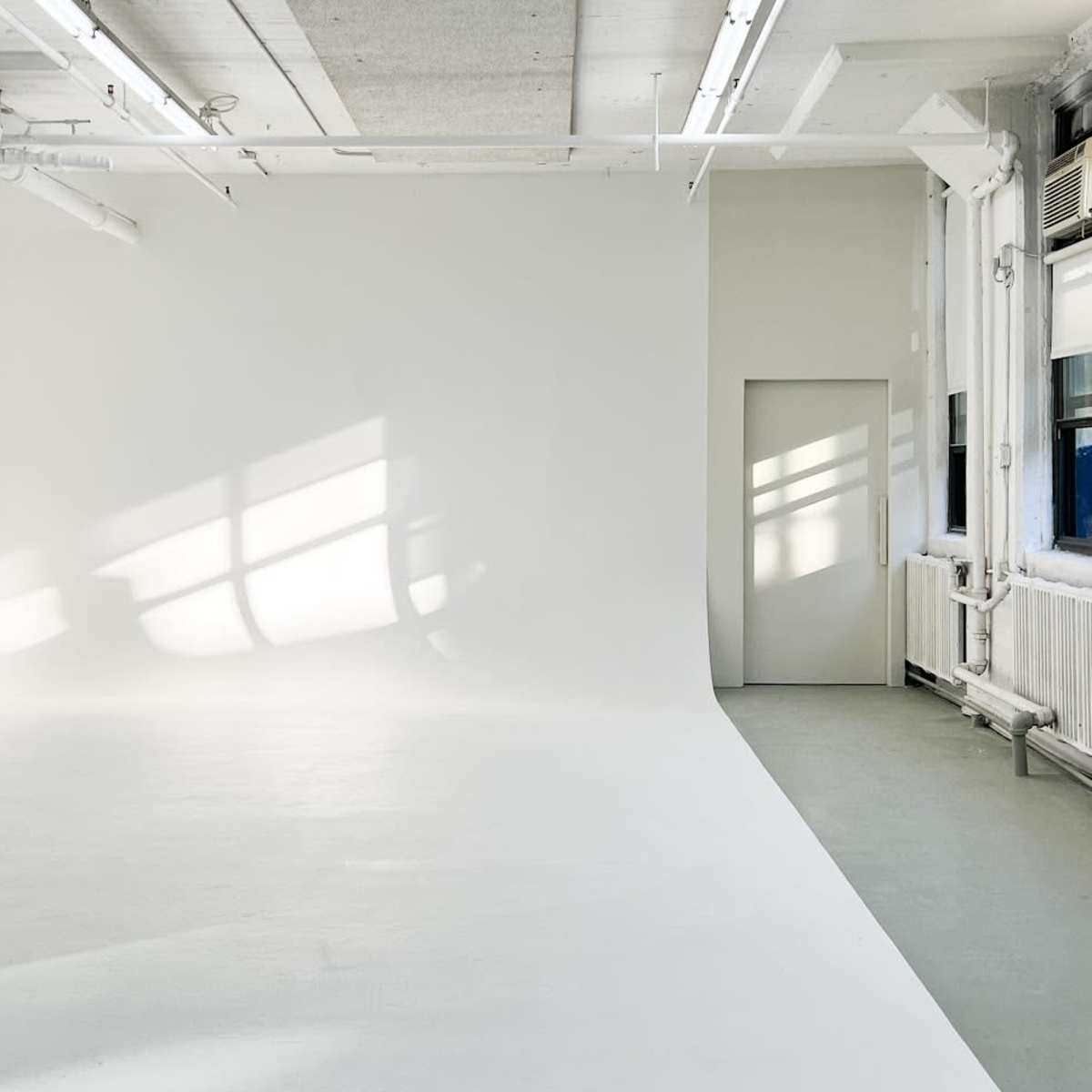 An empty, well-lit studio space with white walls and a door on the right.
