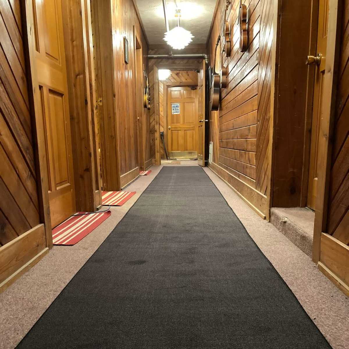 A long, dark carpet runner extends down a well-lit corridor lined with wooden walls and doors.
