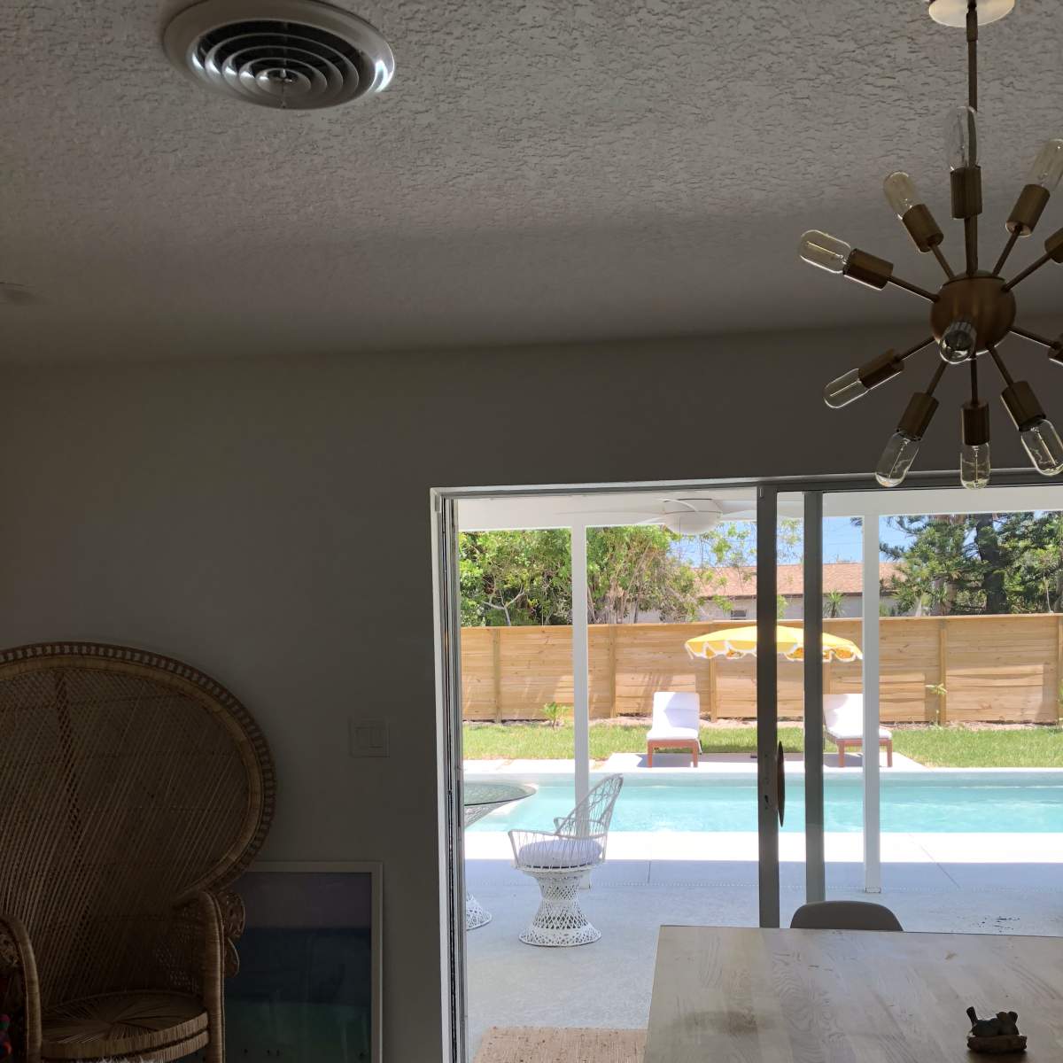 A spacious indoor area features a dining table and a large chair, with sliding glass doors opening to a patio and pool area.