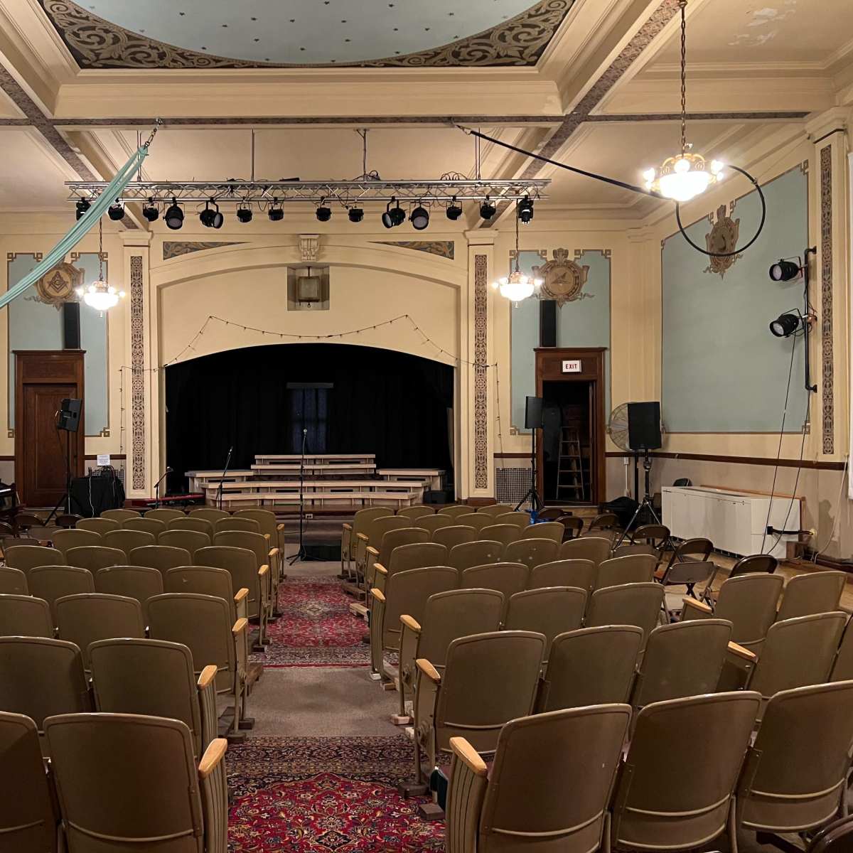 A theater interior with rows of empty seats facing a stage equipped with curtains and lighting fixtures.
