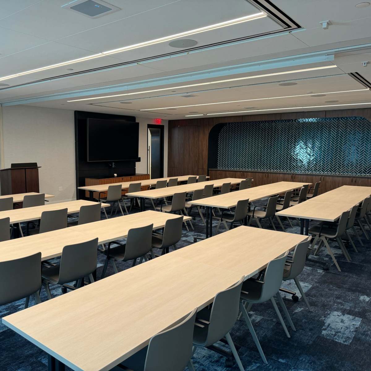 A conference room with multiple rows of tables and chairs arranged for a meeting, featuring a large screen at the front.