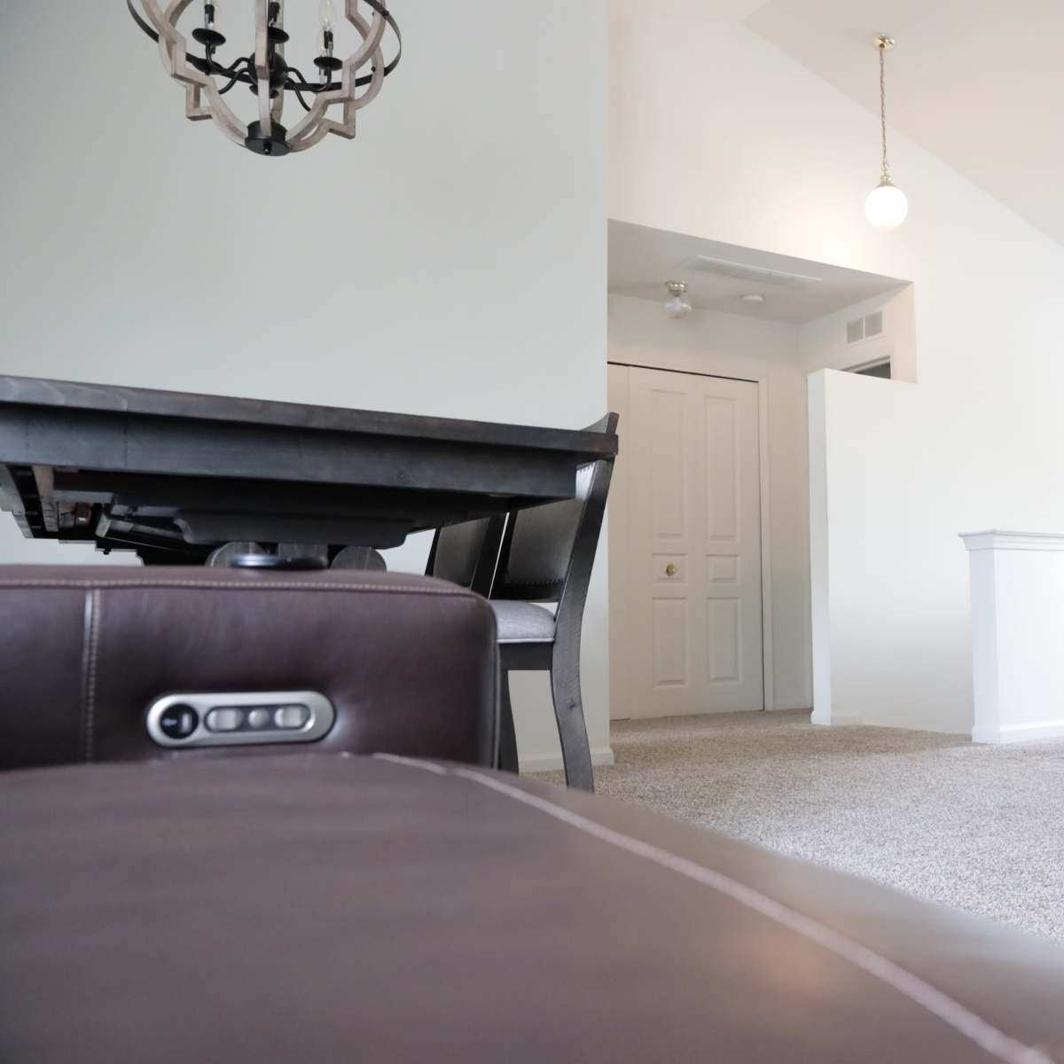 A living area with a dark couch in the foreground, a dining table to the left, and a doorway leading to a bright, open space beyond.
