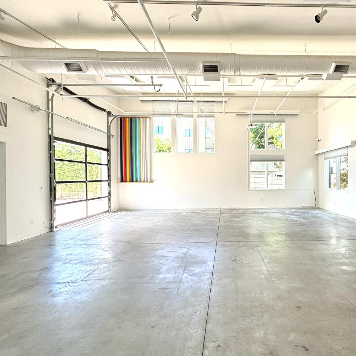A spacious, industrial-style room with concrete flooring, large windows on one wall, and colorful vertical blinds.
