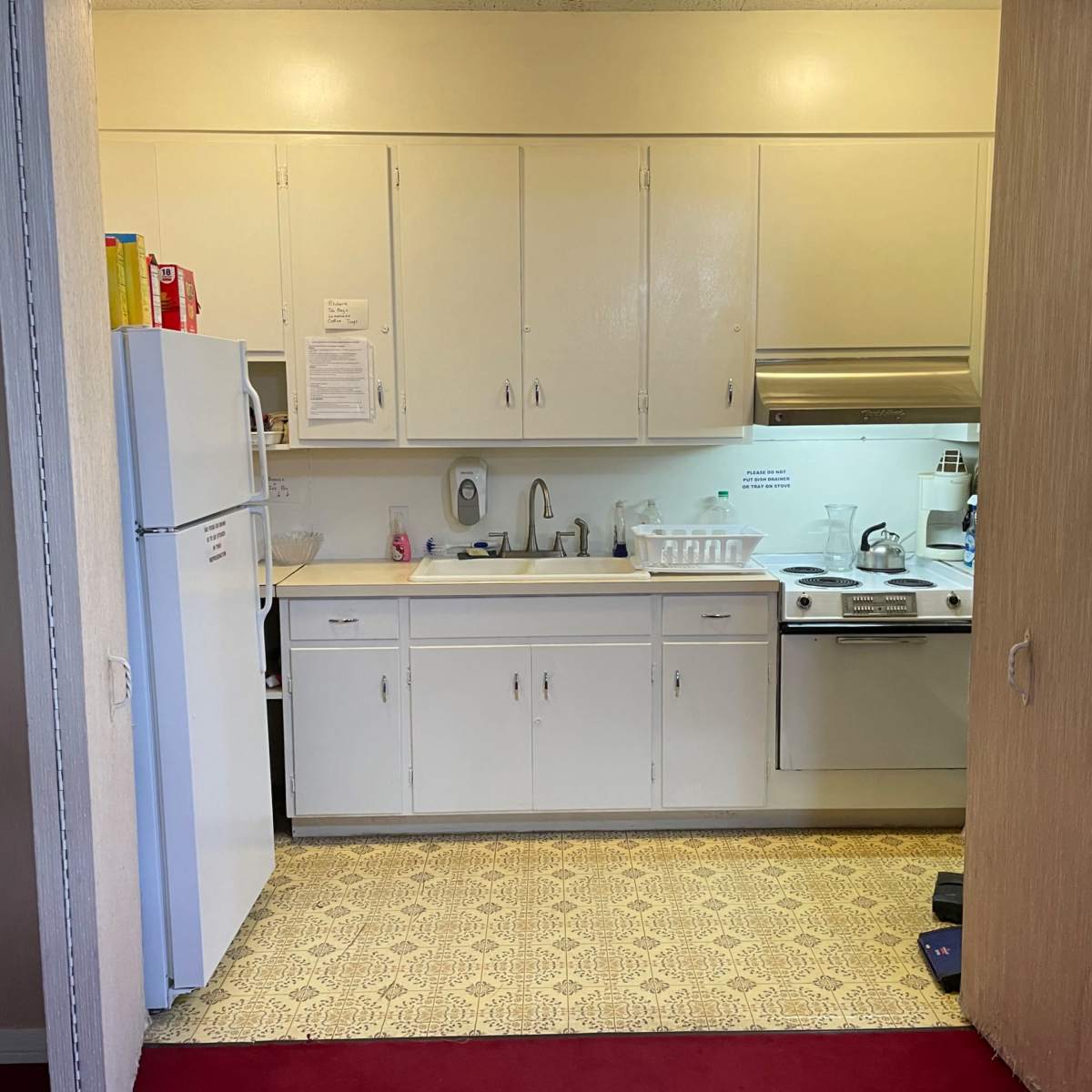 A compact kitchen with white cabinets, a sink, stove, and refrigerator is visible through an open doorway.