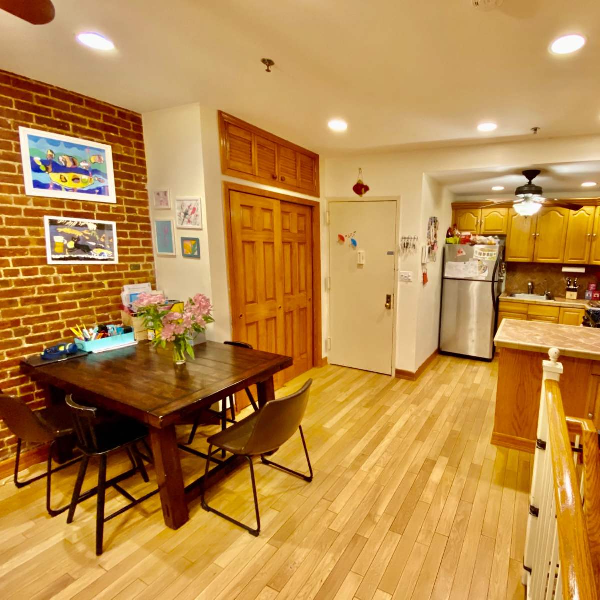 A kitchen and dining area with wooden floors, brick walls, and a table with chairs near a fully-equipped kitchen featuring wooden cabinets and appliances.