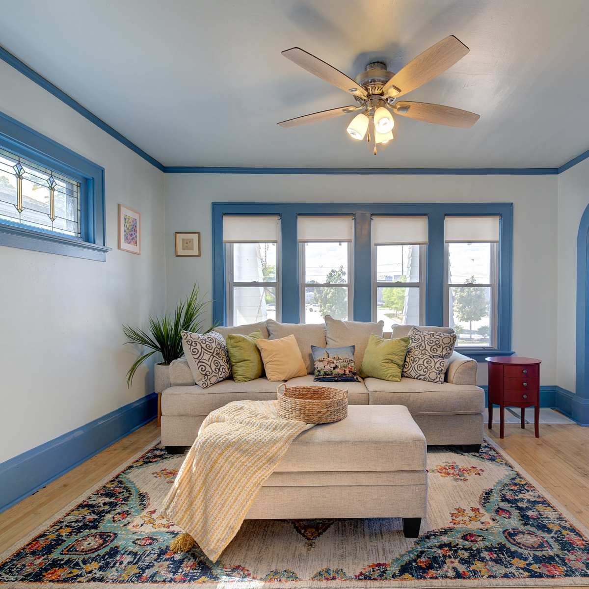 A brightly lit living room featuring a gray sofa adorned with decorative pillows, a coffee table, and an entrance with a black door.