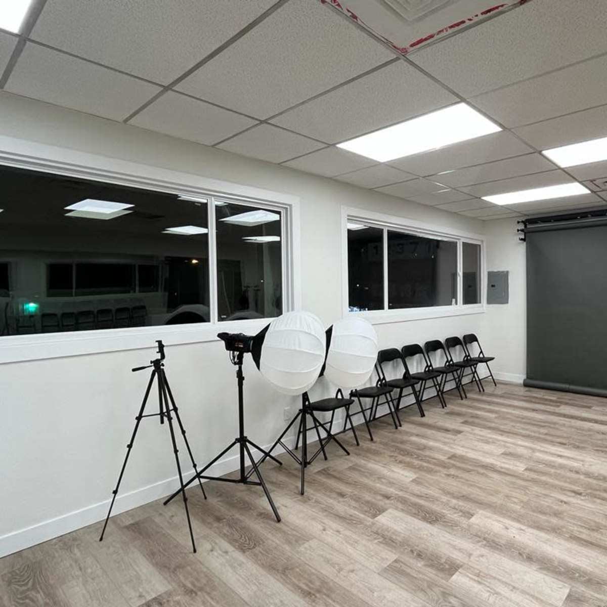 A well-lit studio space with a green backdrop, tripods, light modifiers, and folding chairs arranged against the wall.
