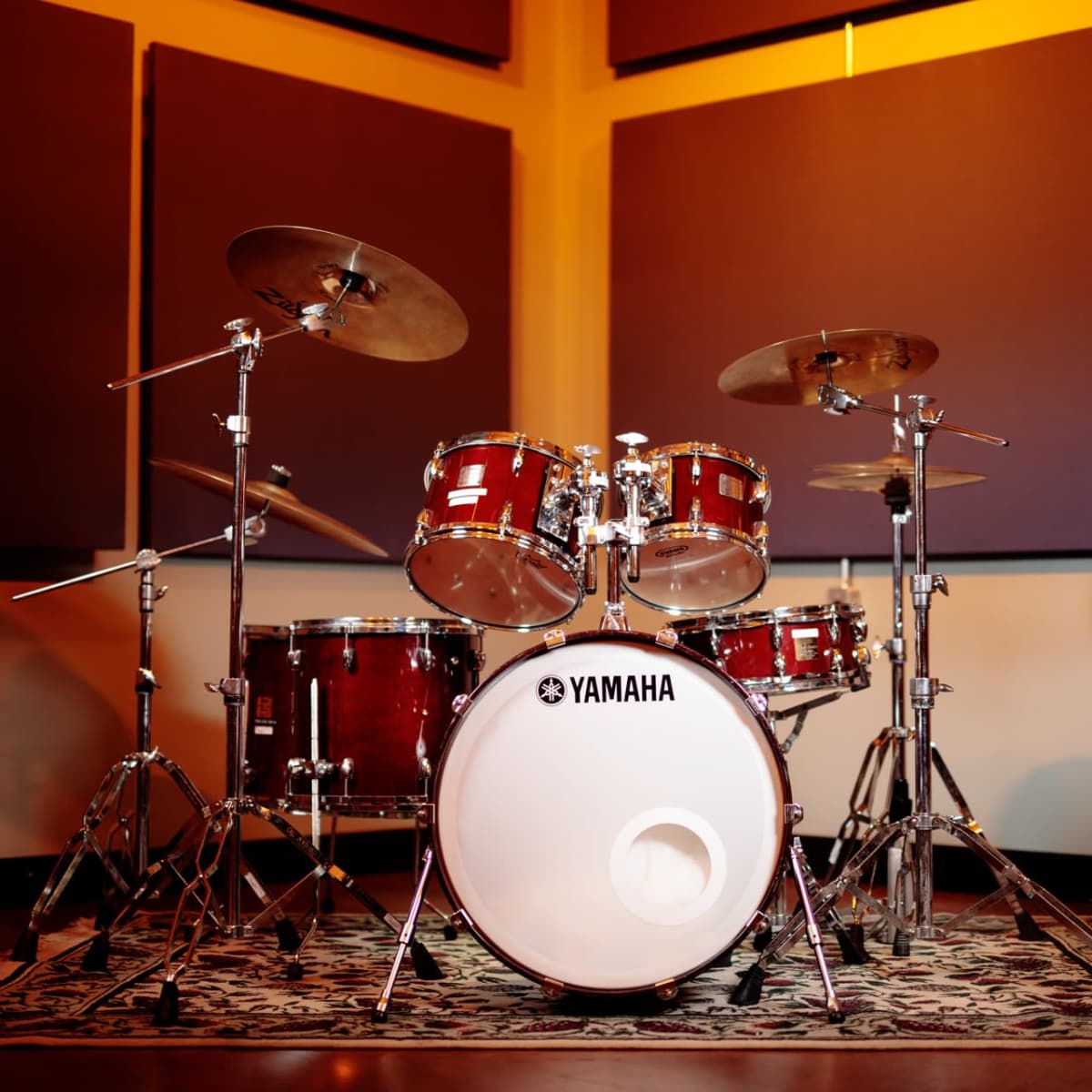 A Yamaha drum set is positioned in a soundproof studio with a patterned rug on the floor.