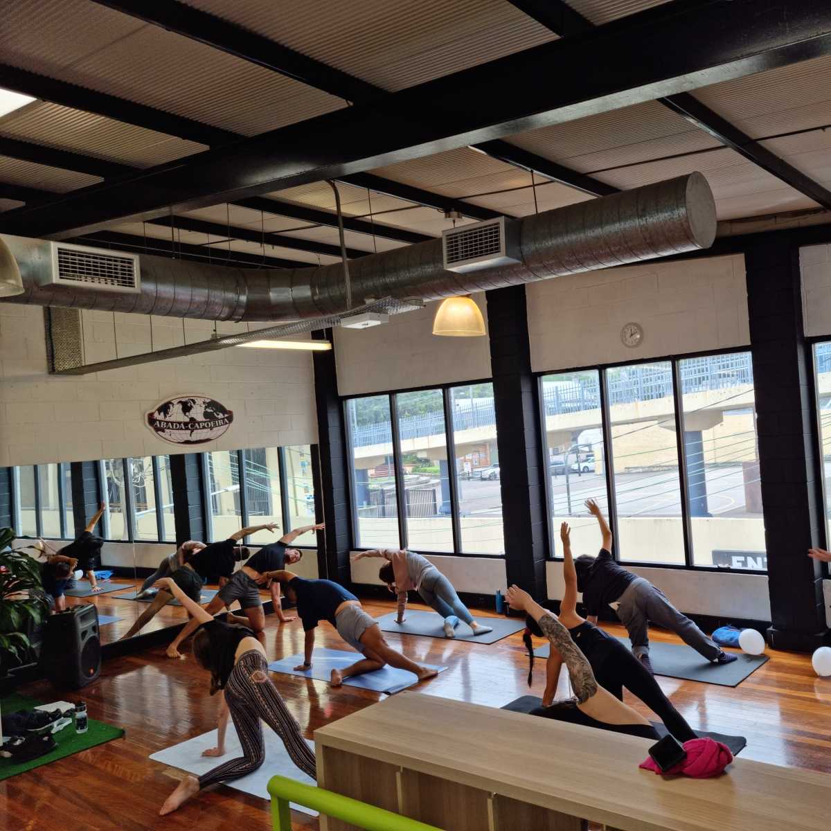 A group of people are practicing yoga in a spacious studio with large windows and wooden floors.