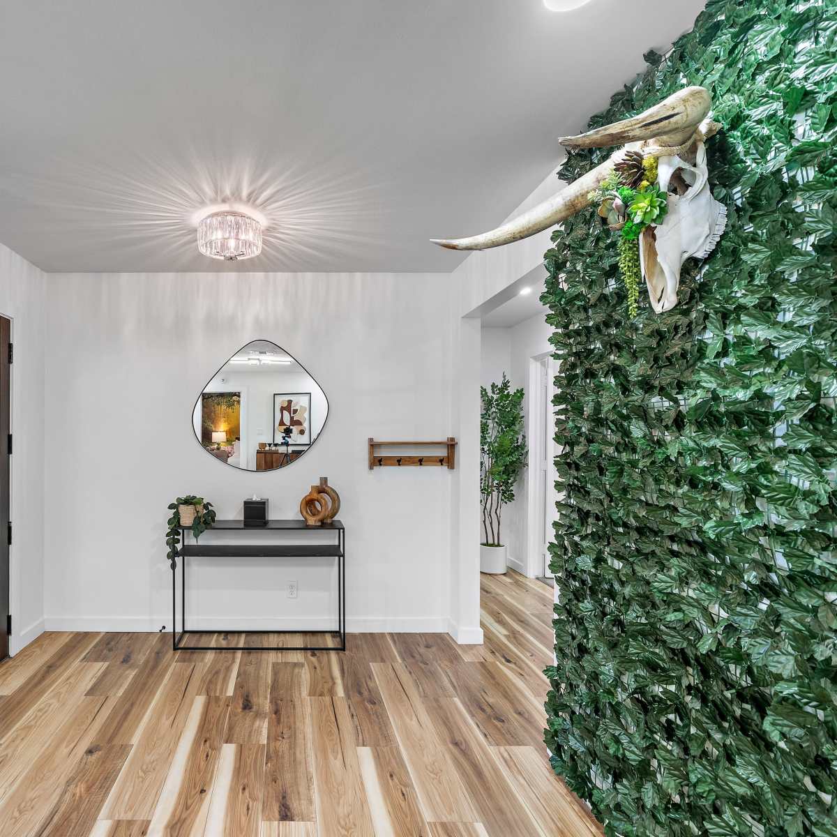A modern entryway featuring a green leaf-covered wall, a decorative mirror above a table, and a door to the left.
